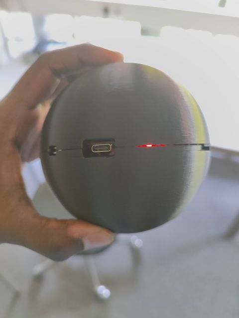 SPP Smart Ball prototype held in a hand, showing its spherical enclosure, USB connector, and illuminated red indicator
